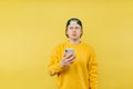 Young man in a yellow sweatshirt stands with a smartphone in his hands on a yellow background and looks away with a serious face Royalty Free Stock Photo