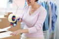 Young manager with packaging tape gun dispenser sealing one of boxes Royalty Free Stock Photo