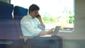 Young manager wearing a white shirt and jeans is riding a train to work and using his laptop.