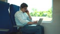 Young manager wearing a white shirt and jeans is riding a train to work and using his laptop.