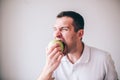 Young manin white shirt isolated over background. Guy biting piece of green fresh tasty apple. Delicious yummy fruit. Royalty Free Stock Photo
