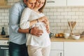 Young married couple embraces standing near table in kitchen. Husband hugs his pregnant wife. Lifestyle, happy people. Royalty Free Stock Photo