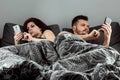 Young married couple are sitting in smartphones lying in their bed. The concept of apathy in relationships, boredom, problems,