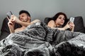 Young married couple are sitting in smartphones lying in their bed. The concept of apathy in relationships, boredom, problems,