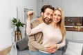 Young married couple smiling cheerfully and showing keys from a new apartment, hugging and looking at camera, standing Royalty Free Stock Photo