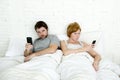 Young married couple using their mobile phone in bed ignoring each other in relationship communication problems Royalty Free Stock Photo