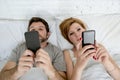 Young married couple using their mobile phone in bed ignoring each other in relationship communication problems Royalty Free Stock Photo