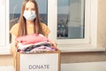 A young masked woman holds a box of donate clothing for charity and helping homeless people