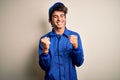 Young mechanic man wearing blue cap and uniform standing over isolated white background very happy and excited doing winner Royalty Free Stock Photo