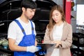 Young mechanic talking to customer asian woman about car with repairing in garage, auto service. Royalty Free Stock Photo