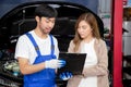 Young mechanic talking to customer asian woman about car with repairing in garage, auto service. Royalty Free Stock Photo