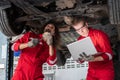 Young mechanics team in uniform are working in auto service with lifted vehicles. Car repair and maintenance concepts Royalty Free Stock Photo