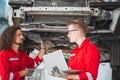 Young mechanics team in uniform are working in auto service with lifted vehicles. Car repair and maintenance concepts Royalty Free Stock Photo