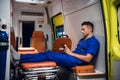 Young medical worker in a blue uniform checking his messages on the phone, while sitting in the ambulance car Royalty Free Stock Photo