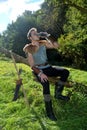 Young Medieval dressed man, sits on branch, drinks from drinking horn