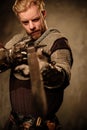 Young medieval knight posing on dark background.