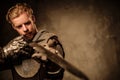 Young medieval knight posing on dark background.