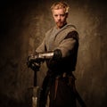 Young medieval knight posing on dark background.