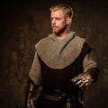 Young medieval knight posing on dark background.