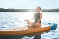 Young meditating yoga on color SUP board on river at sunset