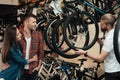 A young man with a beard shows a man and a woman a wheel from a bicycle in a bicycle shop.