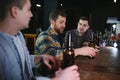 Young men in casual clothes are talking, laughing and drinking while sitting at bar counter in pub Royalty Free Stock Photo