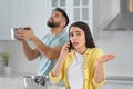 Young man collecting leaking water from ceiling while girlfriend calling roof repair service in kitchen Royalty Free Stock Photo