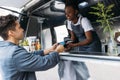 Young man with credit card paying to a saleswoman at a food truck. Female entrepreneur in apron receiving payment from a customer