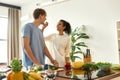 Young man cutting vegetables while woman feeding him a slice of cucumber. Vegetarians preparing healthy meal in the Royalty Free Stock Photo