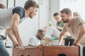 young men with facial expression playing table football with friends sitting