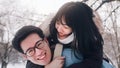 Young man giving piggyback ride to his girlfriend in the park on snowy winter day. Newlywed asian couple having fun Royalty Free Stock Photo