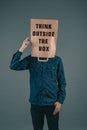 Young men has a paper bag on his head, the phrase think outside the box is standing on it, brainstorming for new ideas