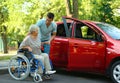 Young man helping disabled senior woman in wheelchair to get into car