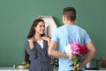 Young man hiding flowers for girlfriend behind his back indoors