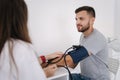 Young man with high blood pressure. Female doctor using sphygmomanometer with stethoscope checking blood pressure to a Royalty Free Stock Photo