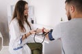 Young man with high blood pressure. Female doctor using sphygmomanometer with stethoscope checking blood pressure to a Royalty Free Stock Photo