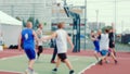 Young men play basketball on fenced sports ground