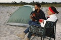 Young man playing guitar to his beloved girlfriend near camping tent on beach Royalty Free Stock Photo