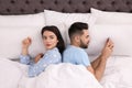 Young man preferring smartphone over his girlfriend in bed at home