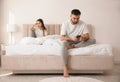 Young man preferring smartphone over girlfriend on bed at home. Relationship problems