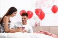 Young man presenting gift to his girlfriend in decorated with air balloons. Celebration of Saint Valentine`s Day Royalty Free Stock Photo