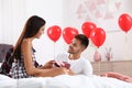 Young man presenting gift to his girlfriend in bedroom. Celebration of Saint Valentine`s Day Royalty Free Stock Photo