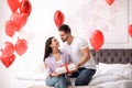 Young man presenting gift to his girlfriend in bedroom decorated with heart balloons. Valentine`s day celebration Royalty Free Stock Photo