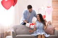 Young man presenting gift to his girlfriend in room decorated with heart shaped balloons. Valentine`s day celebration Royalty Free Stock Photo