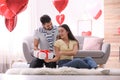 Young man presenting gift to his girlfriend in room decorated with heart shaped balloons. Valentine`s day celebration Royalty Free Stock Photo