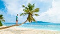 Young men relaxing at a palm tree on a tropical white beach at the La Digue Seychelles Islands