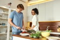 Young man smiling, cutting vegetables while woman talking and watching him. Vegetarians preparing healthy meal in the Royalty Free Stock Photo