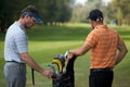Young men standing in golf course by golf bag full of sticks Royalty Free Stock Photo