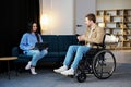 Young man in wheelchair holding mobile phone in hands and his wife using laptop at home Royalty Free Stock Photo