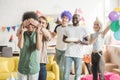 Young men and women covering eyes of young female friend and greeting her with birthday cake